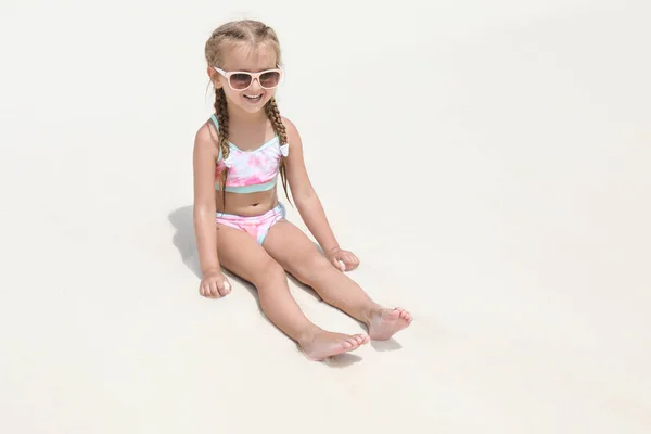 Cute little girl sitting on beach sand at sea resort — Stock Photo, Image