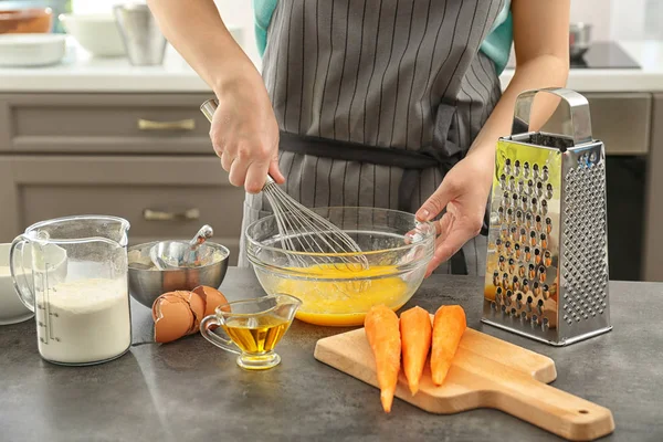 Mujer joven batiendo huevos para pastel de zanahoria en la cocina — Foto de Stock