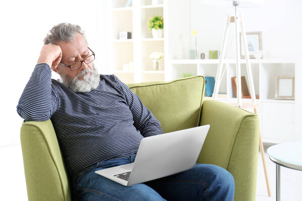 Handsome elderly man sitting in armchair with laptop