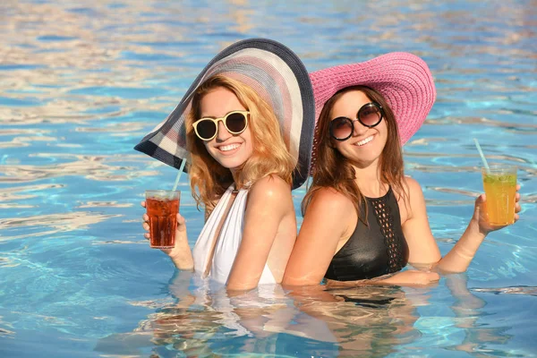 Dos hermosas mujeres con cócteles relajándose en la piscina — Foto de Stock