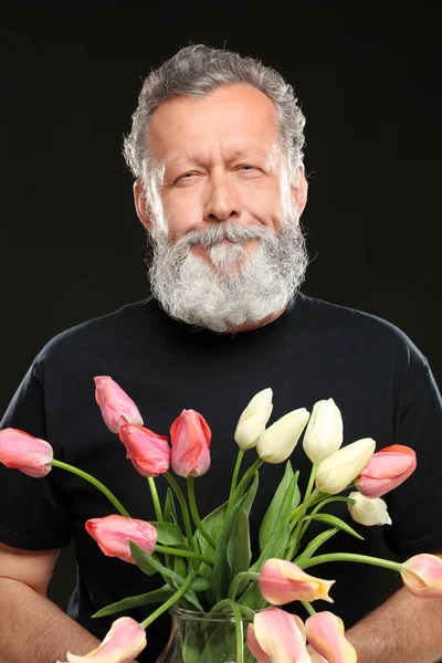 Knappe oudere man met tulpen op zwarte achtergrond — Stockfoto