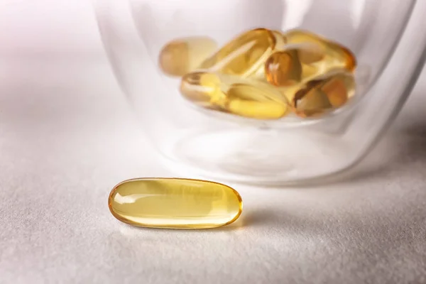 Glass with fish oil capsules on light background — Stock Photo, Image