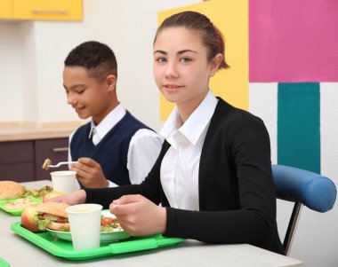 Öğle Yemeği yerken okul kafeteryasında masada oturan çocuk