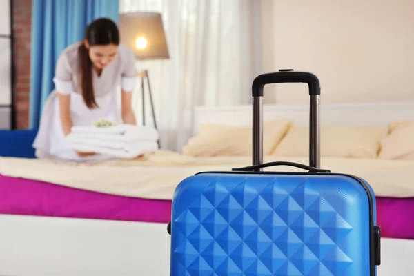 Blue suitcase in light hotel room and blurred maid on background — Stock Photo, Image