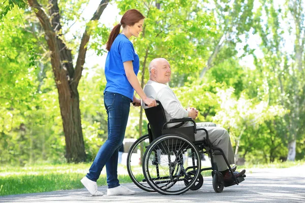 Feliz hombre mayor en silla de ruedas con una joven voluntaria al aire libre — Foto de Stock