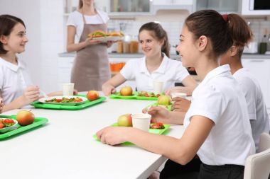 Öğle Yemeği yerken okul kafeteryasında masada oturan çocuk