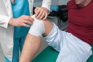 Orthopedist applying bandage onto patient's leg in clinic clipart