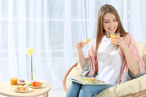 Ung vacker kvinna äter frukost i fåtölj — Stockfoto