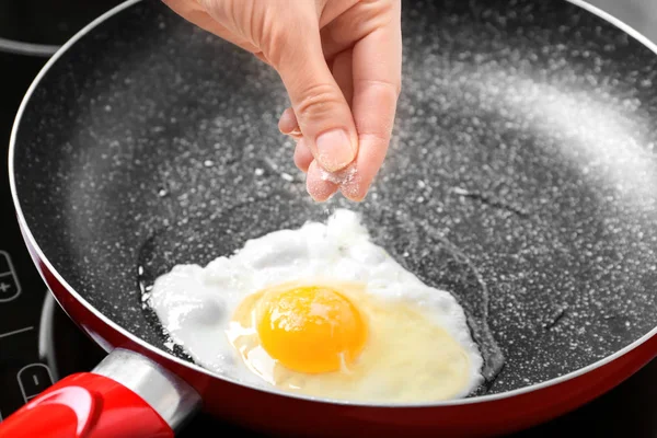 Hand adding salt to egg — Stock Photo, Image
