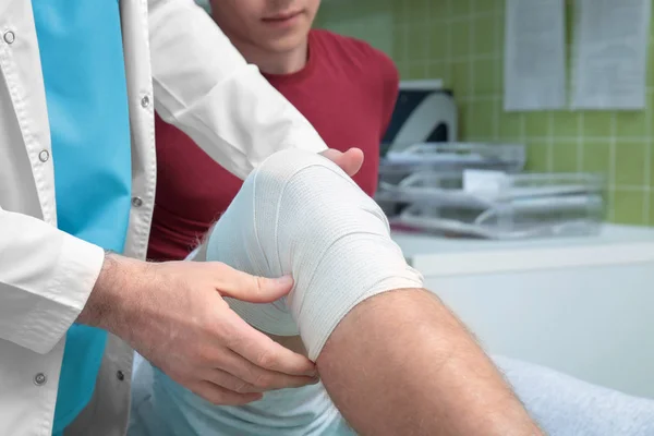 Ortopedista aplicando vendaje en la pierna del paciente en la clínica —  Fotos de Stock