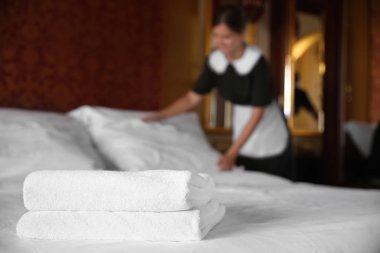 Yatak otel odası ve arka plan üzerinde bulanık oda hizmetçisi temiz beyaz havlu