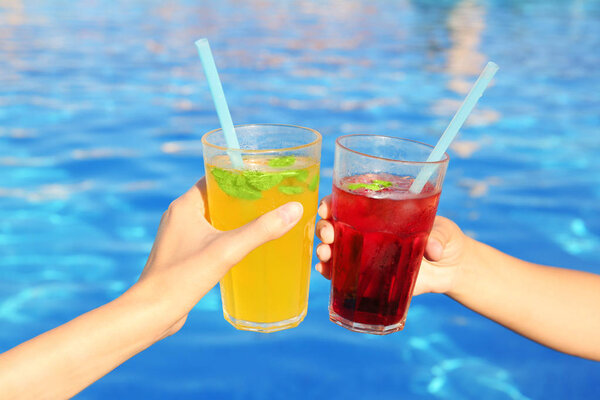 Hands of young women clinking glasses with cocktails near pool