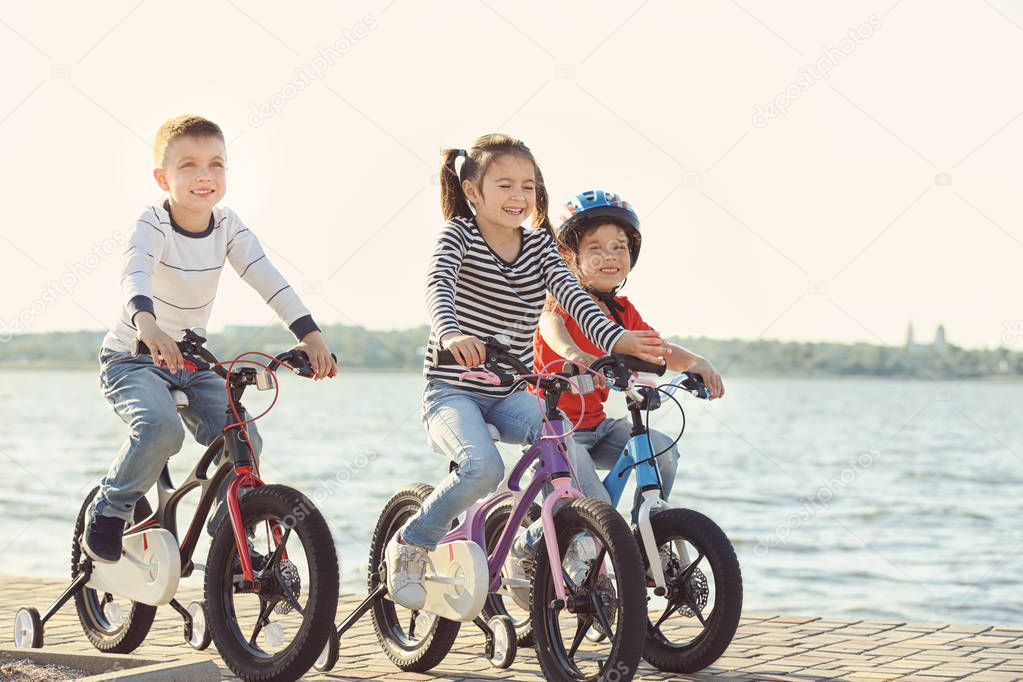 Cute little children riding bicycles near river on sunny day