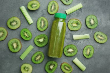 Dilimlenmiş yeşil olgun kivi, sap kereviz ve güler yüzlü şişeyle gri arka plan üzerinde
