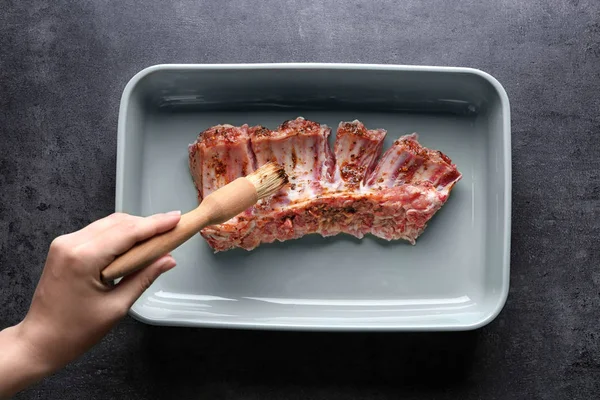 Hand of young woman adding spices to raw pork ribs in kitchen — Stock Photo, Image