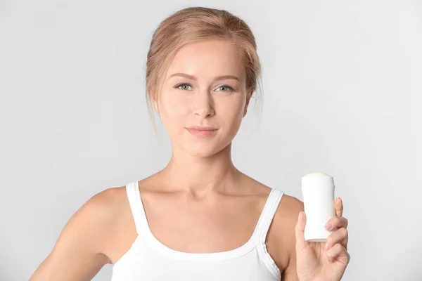 Mooie jonge vrouw met deodorant op lichte achtergrond — Stockfoto
