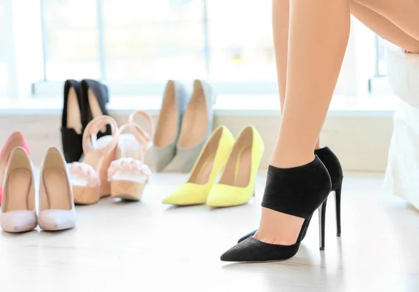 Young woman with slim legs having rest in light room with different shoes — Stock Photo, Image