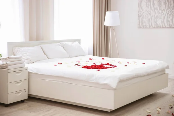 Pétalos de rosa en la cama en la habitación de hotel — Foto de Stock