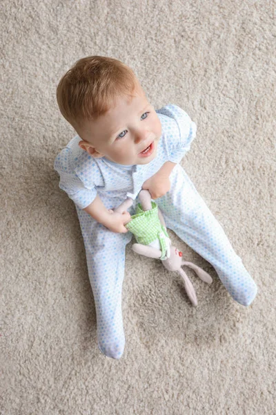 Lindo bebé niño sentado en la alfombra y jugando con el conejo cerca de punto húmedo —  Fotos de Stock