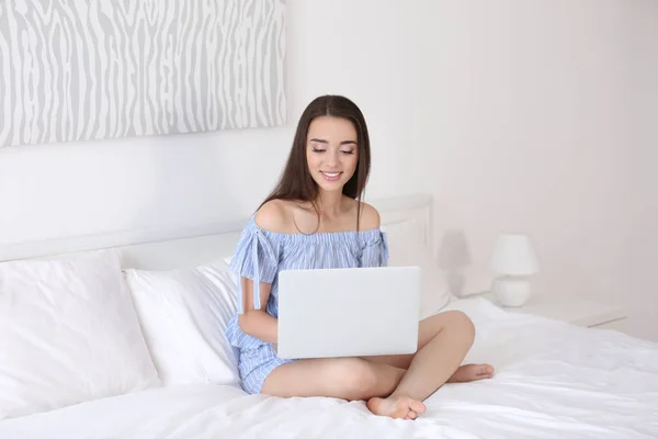 Mujer hermosa joven usando el ordenador portátil en la cama en la habitación de hotel de luz — Foto de Stock