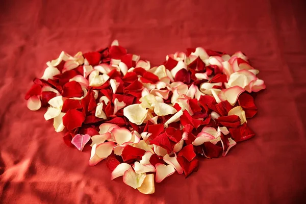 Heart made of rose petals on bed in hotel room — Stock Photo, Image