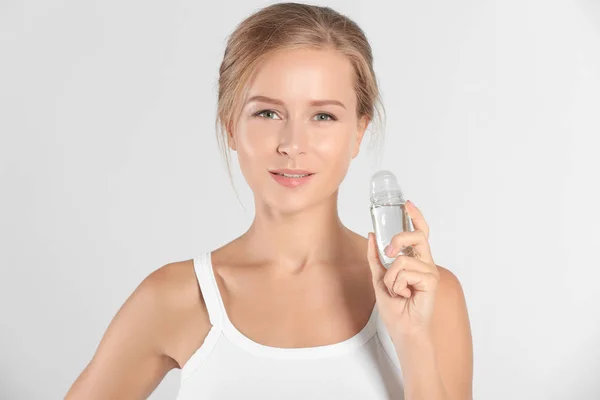 Mooie jonge vrouw met deodorant op lichte achtergrond — Stockfoto