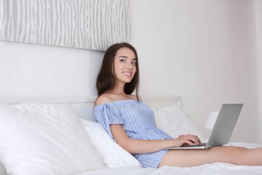 Işık otel odasında yatakta dizüstü bilgisayar kullanan genç güzel kadın