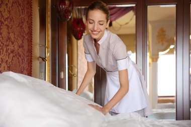 Oda hizmetçisi otel odasında yatak yapıyor.