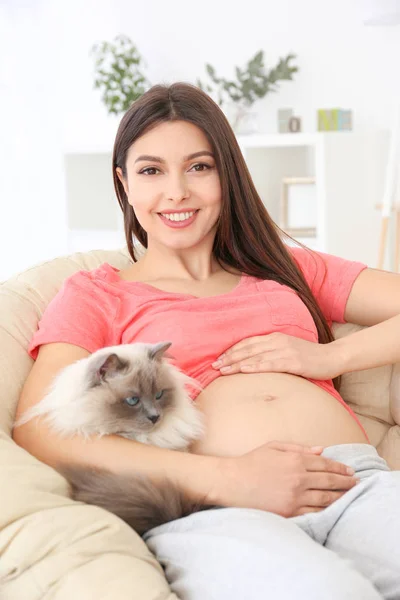 Unga gravid kvinna sitter med söt katt i fåtölj — Stockfoto