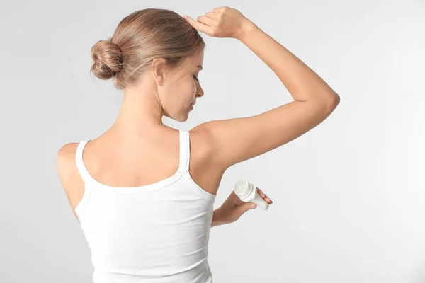 Mooie jonge vrouw met deodorant op lichte achtergrond — Stockfoto