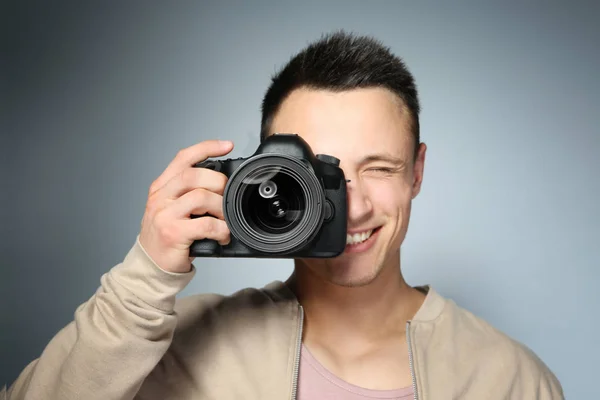 Schöner Fotograf mit Kamera auf grauem Hintergrund — Stockfoto