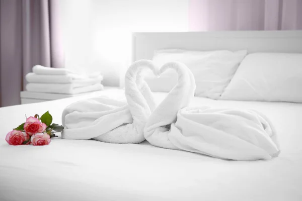 Dois cisnes de toalha e buquê de rosas na cama no quarto do hotel — Fotografia de Stock