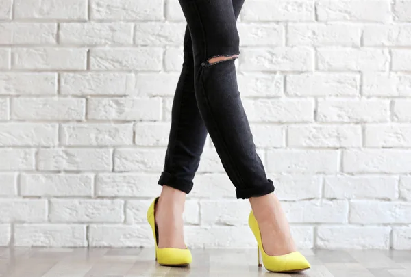Ноги молодой женщины на высоких каблуках и джинсах, стоящие у стены из белого кирпича — стоковое фото
