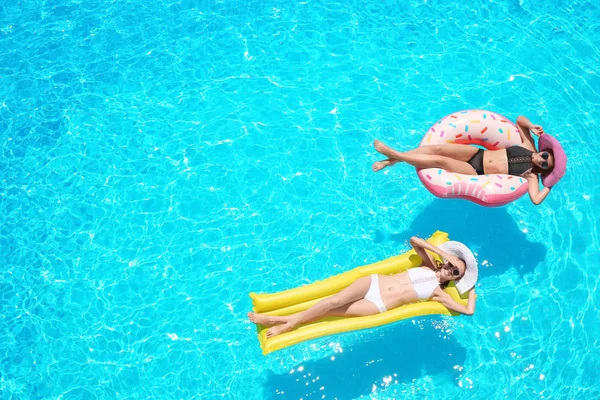 Mooie jonge meisjes met opblaasbare donut en matras in blauwe zwembad — Stockfoto