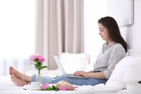 Güzel genç kız otel odasında yatakta bir dizüstü bilgisayar kullanarak — Stok fotoğraf