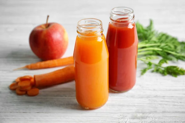 Lahodné šťávy mrkev a rajče v lahvích na dřevěný stůl — Stock fotografie