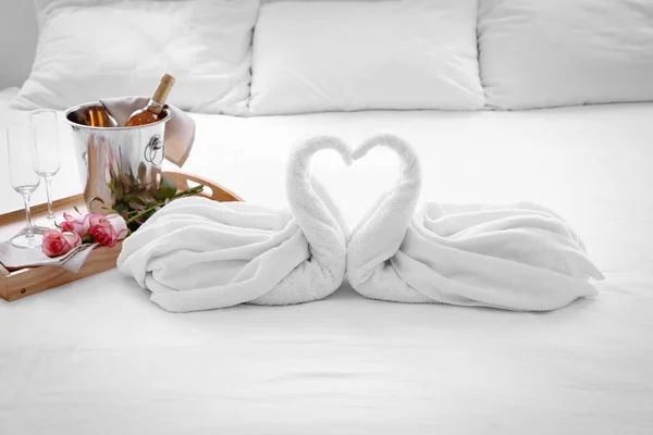 Sammansättning av två handduk svanar, blommor och ishink med champagne på sängen på hotellrummet — Stockfoto