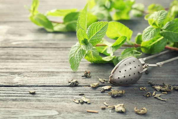 Tea strainer and leaves of lemon balm on wooden table — Stock Photo, Image