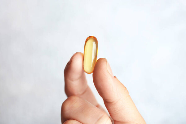Fish oil pill in female hand on light background