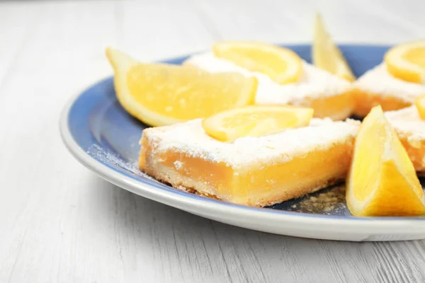 Plate with lemon pie bars on wooden background