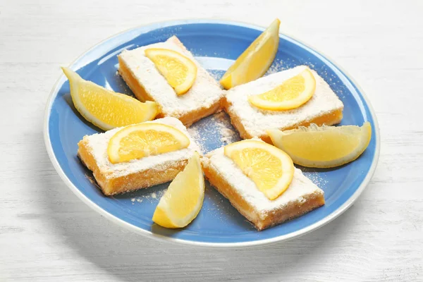 Plate with lemon pie bars on wooden background