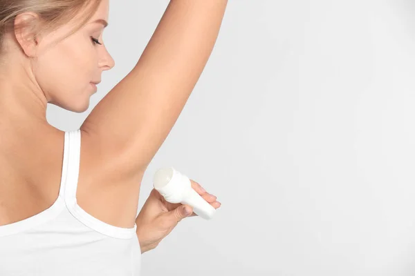 Mooie jonge vrouw met deodorant op lichte achtergrond — Stockfoto