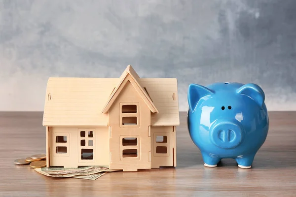 Piggy bank with money and house model on table. Savings concept — Stock Photo, Image