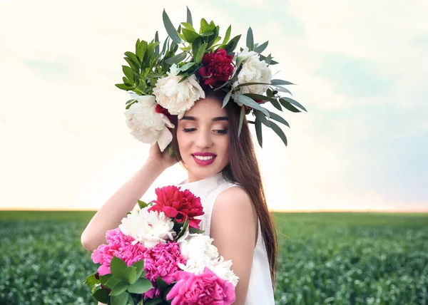 Όμορφη νεαρή γυναίκα που φοράει floral στεφάνι στο πράσινο πεδίο — Φωτογραφία Αρχείου