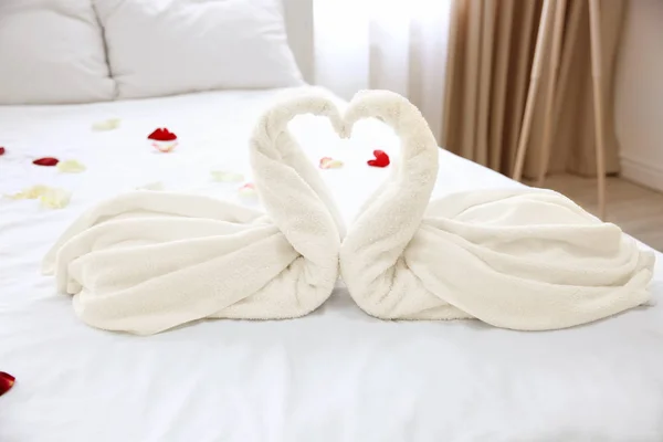 Twee handdoek zwanen en rozenblaadjes op bed in lichte hotelkamer — Stockfoto