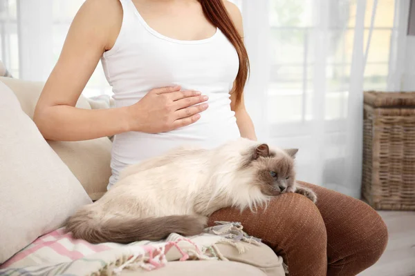 Jovem mulher grávida com gato bonito sentado no sofá na sala de luz — Fotografia de Stock