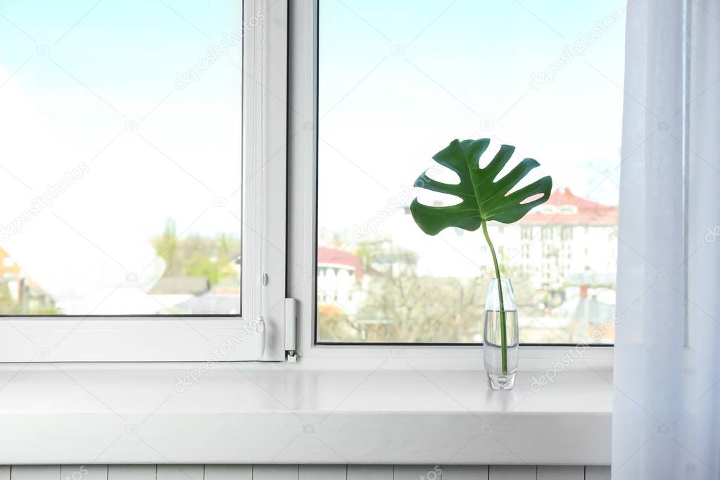 Glass vase with beautiful tropical leaf on window sill