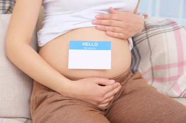 Pregnant woman with paper sticker on tummy, closeup. Concept of choosing baby name clipart