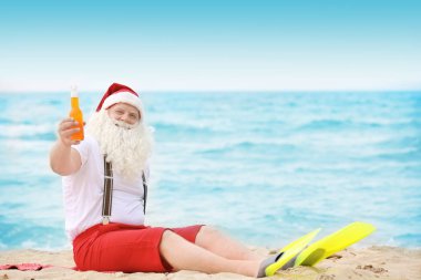 Sahilde oturup içki şişe ile otantik Noel Baba