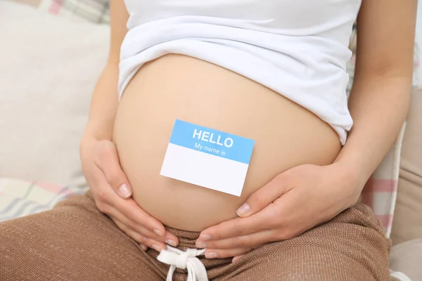 Donna incinta con adesivo di carta sulla pancia, primo piano. Concetto di scegliere il nome del bambino — Foto Stock